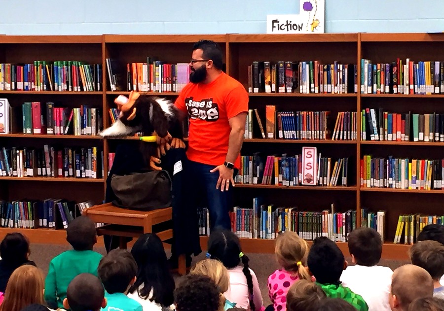 A live ventriloquism performance in a library, in front of the fiction shelves