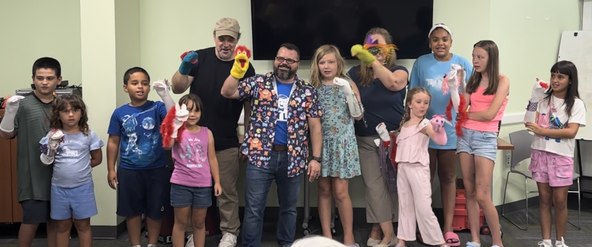 Children performing the ABCs with handmade sock puppets during their first ventriloquism show at a library
